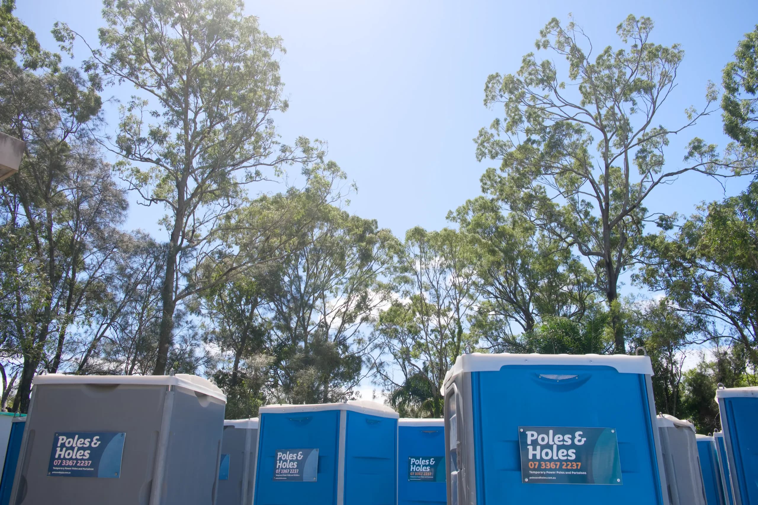 Rows of Poles and Holes branded portable toilets lined up beneath gum trees at the Capalaba depot in South East Queensland